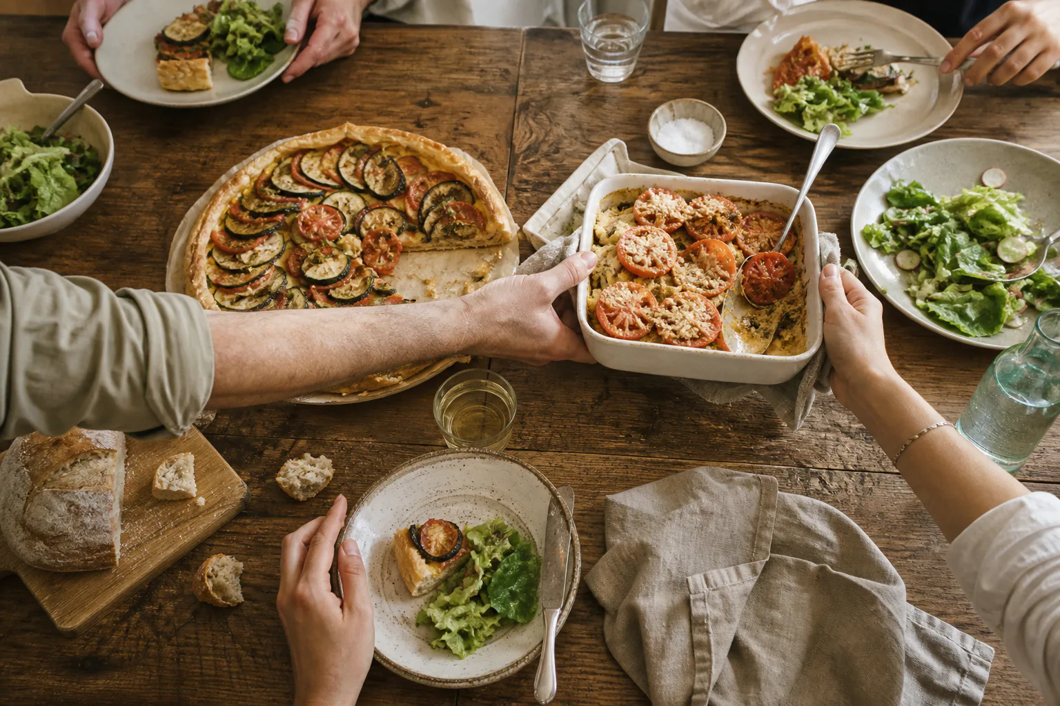 Diners sharing vegetable tarts, a gratin and salads around a table